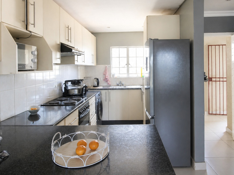 A functional kitchen featuring granite countertops, built-in cabinetry, an electric hob, oven, and a tiled backsplash, offering a practical layout for daily use.