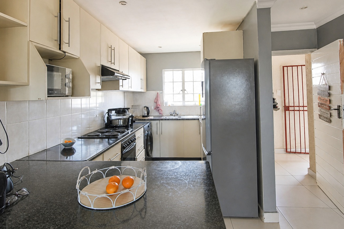 A functional kitchen featuring built-in cabinetry, granite countertops, an electric hob, and a tiled backsplash, with direct access to an adjacent hallway.