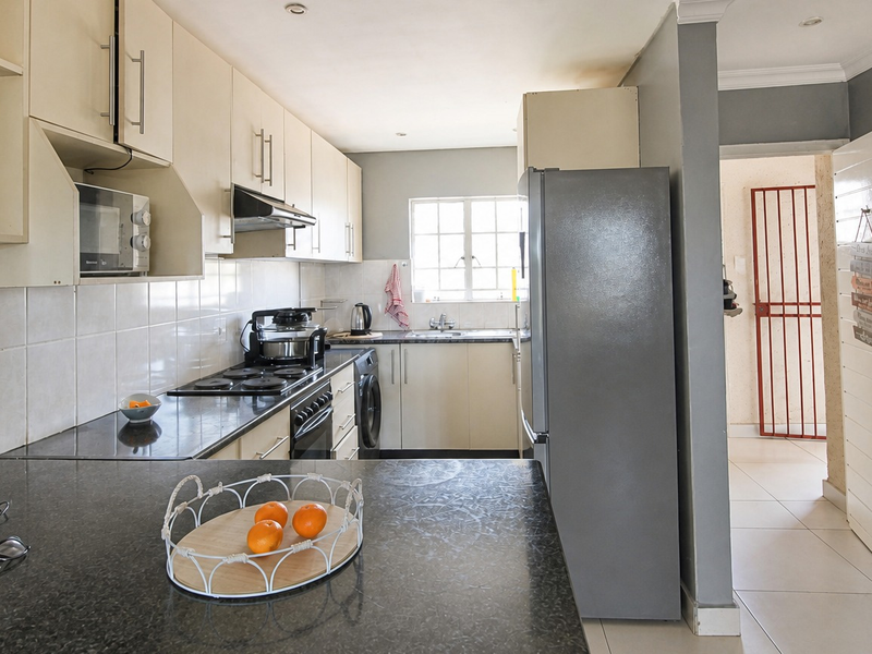 A functional kitchen featuring built-in cabinetry, granite countertops, an electric hob, and a tiled backsplash, with direct access to an adjacent hallway.