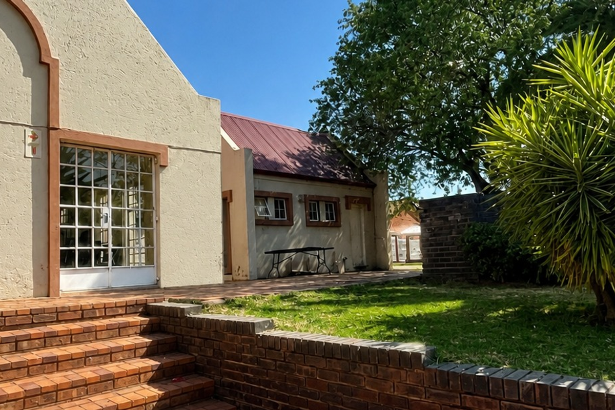 Rear exterior view of the apartment featuring a brick retaining wall, steps, and a small garden area with established trees.