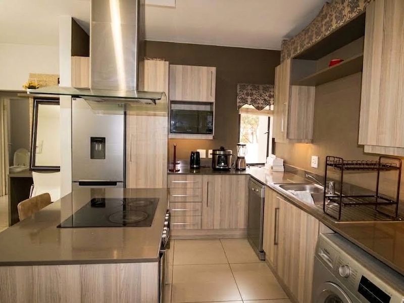 Modern kitchen featuring light wood-grain cabinetry, stone countertops, stainless steel appliances, and a central island with an integrated electric hob.