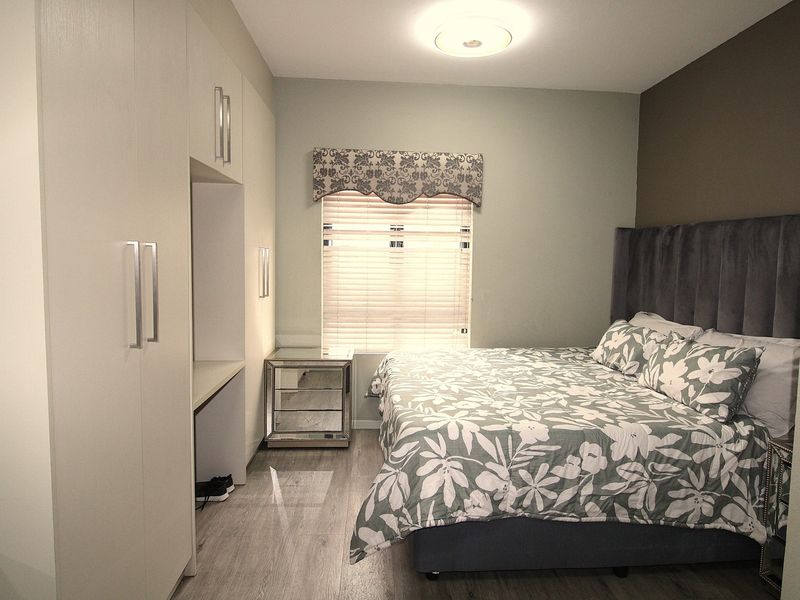 A well-maintained bedroom featuring built-in cupboards, modern laminate flooring, and neutral wall finishes with a functional window treatment.