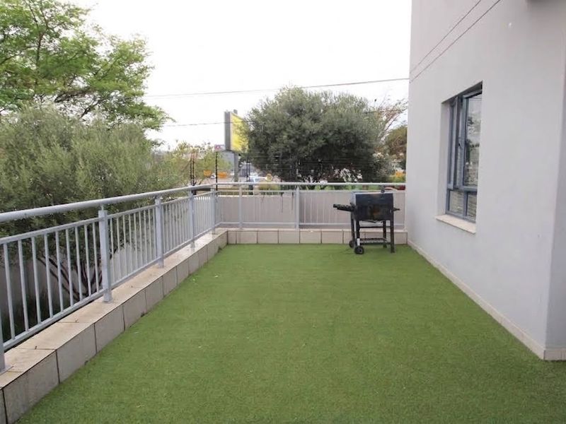 A spacious balcony featuring artificial grass flooring, a secure metal balustrade, and direct access to the apartment interior through an aluminium window.