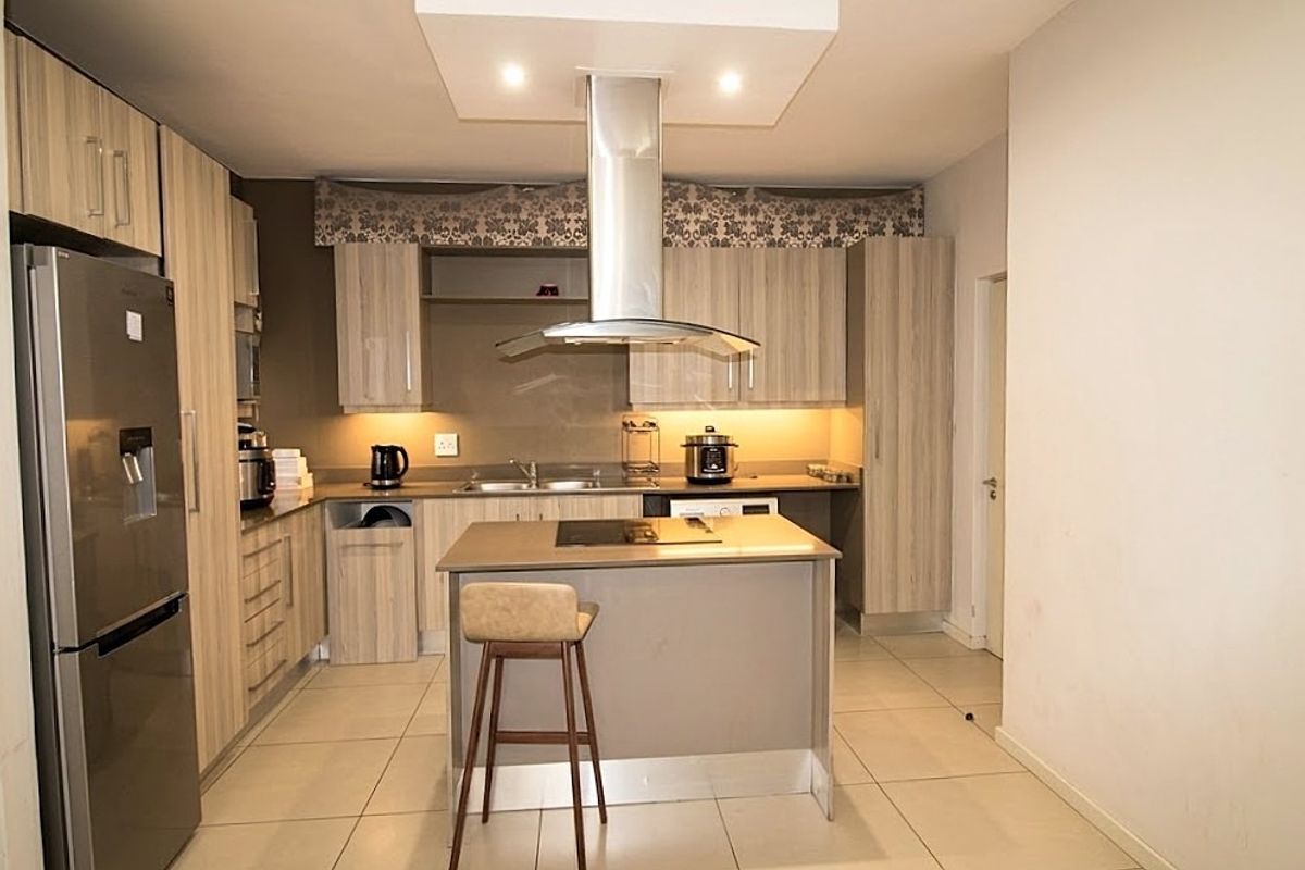 Modern kitchen featuring light wood-finish cabinetry, a central island with a built-in hob, stainless steel extractor fan, and tiled flooring throughout.