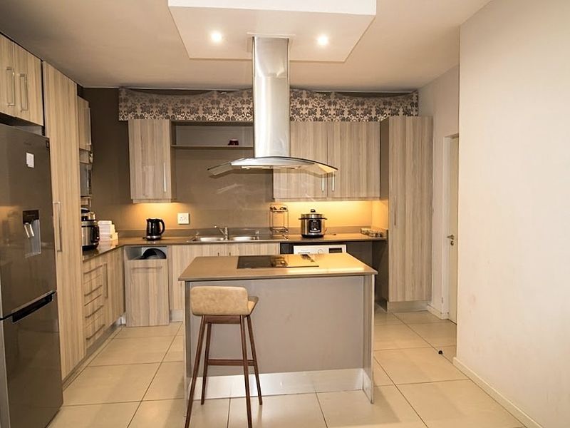 Modern kitchen featuring light wood-finish cabinetry, a central island with a built-in hob, stainless steel extractor fan, and tiled flooring throughout.