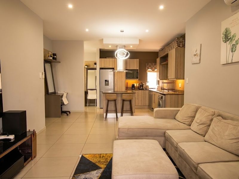 A modern open-plan living and kitchen area featuring tiled floors, recessed lighting, and a functional kitchen island with integrated cabinetry.