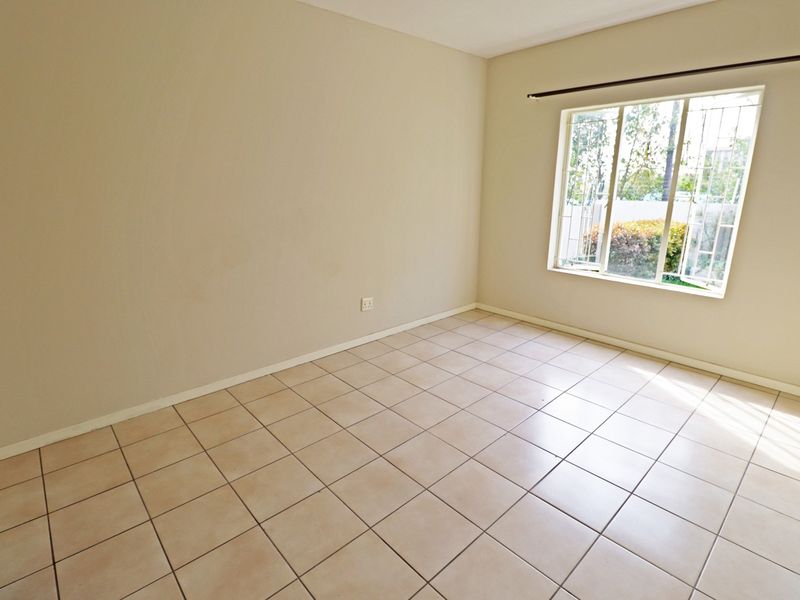A bright, empty bedroom featuring neutral tiled flooring and a window fitted with security bars, offering a clean canvas for personalization.