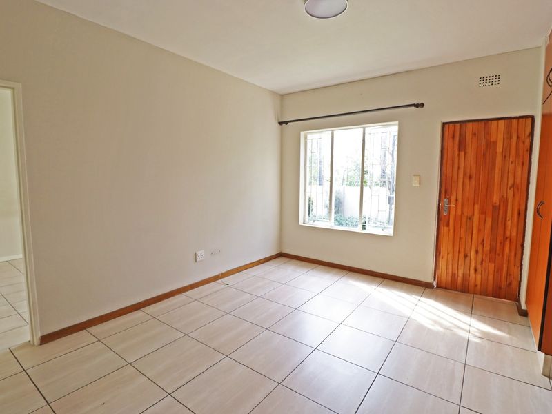 An empty bedroom featuring tiled flooring, built-in wooden cupboards, and a window with security bars, offering a clean and neutral space.