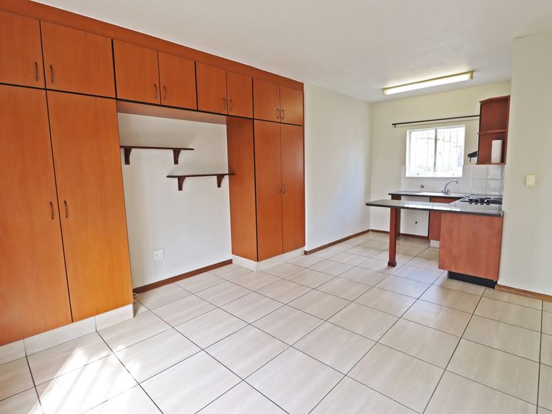 Open-plan kitchen and living area featuring tiled flooring, extensive built-in wooden cabinetry, and a functional kitchen layout with a breakfast counter.