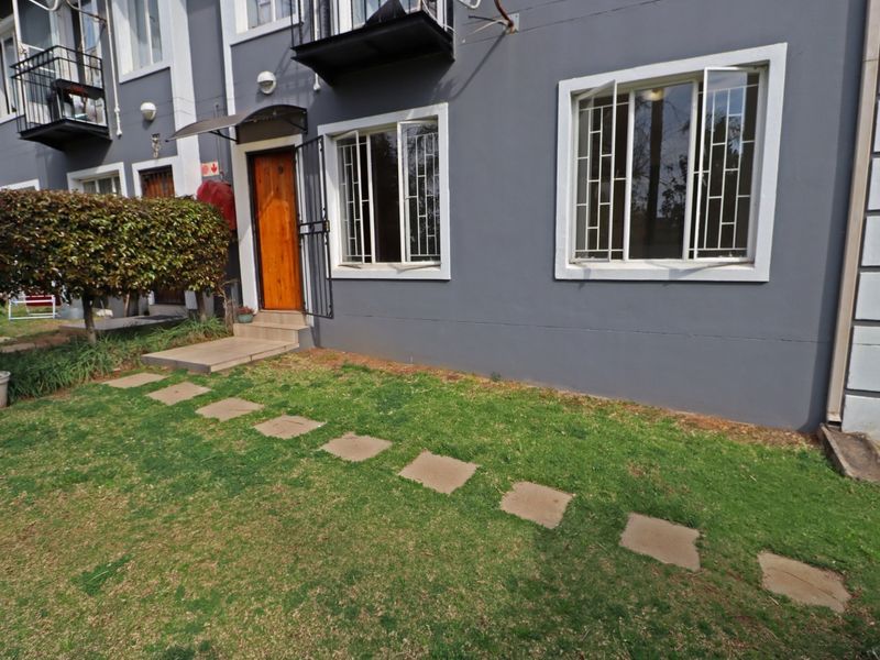 Front exterior view of the apartment featuring a small lawn, paved walkway, security gates, and window bars.