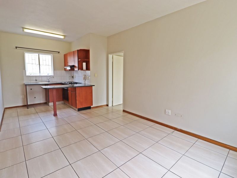 An open-plan living and kitchen area featuring tiled flooring, built-in cabinetry, and a functional kitchen layout in a vacant apartment setting.