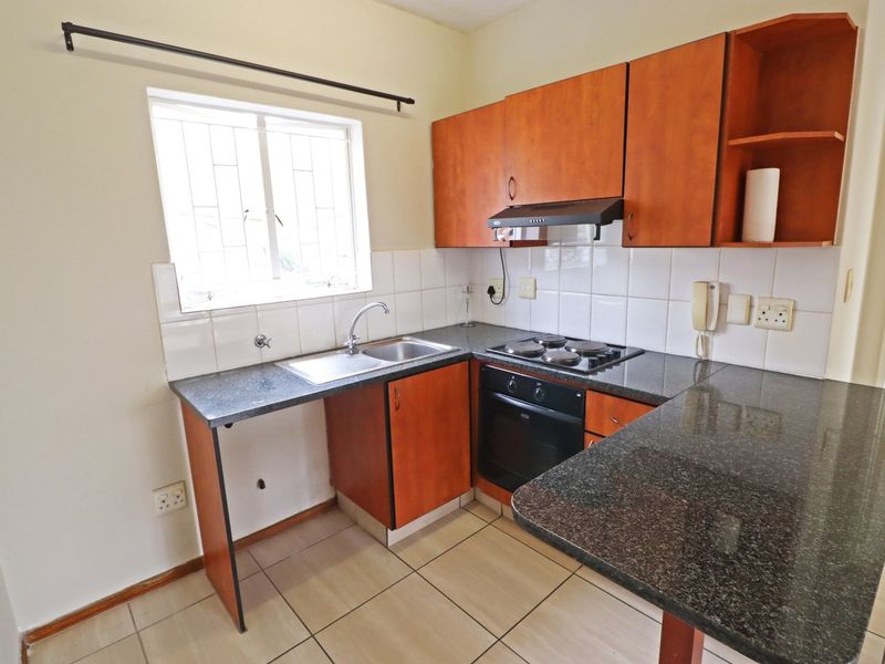 A functional kitchen featuring granite countertops, built-in cabinetry, an electric hob, oven, and tiled finishes, offering a practical layout for daily cooking.