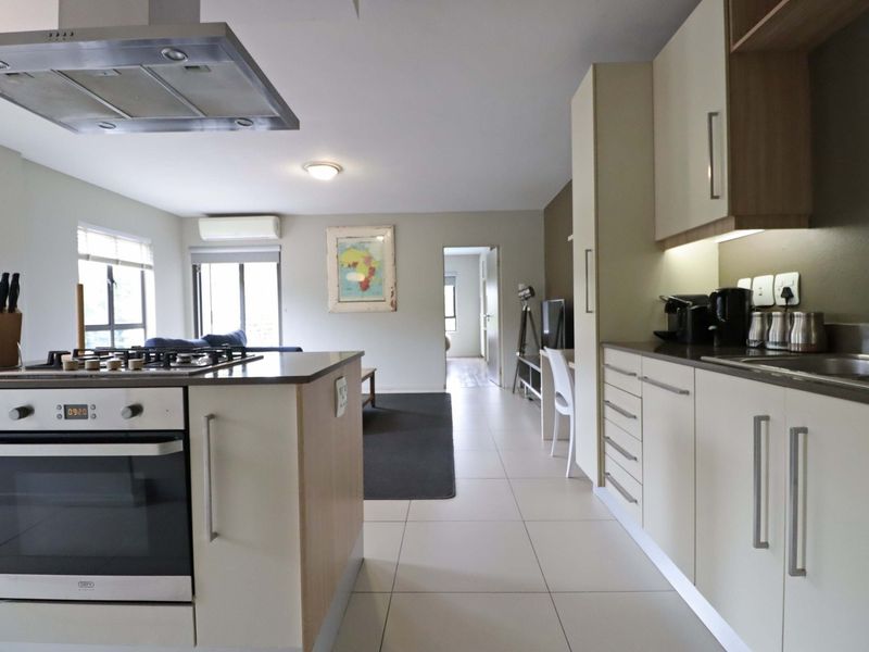 Modern open-plan kitchen and living area featuring sleek cabinetry, stone countertops, integrated appliances, and neutral tiled flooring throughout.