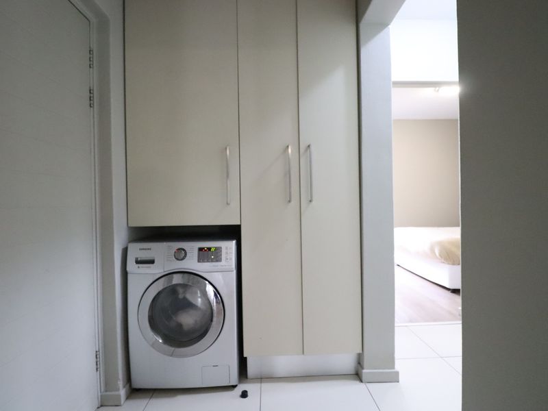 A compact laundry area featuring built-in cabinetry and space for a washing machine, finished with clean tiled flooring.