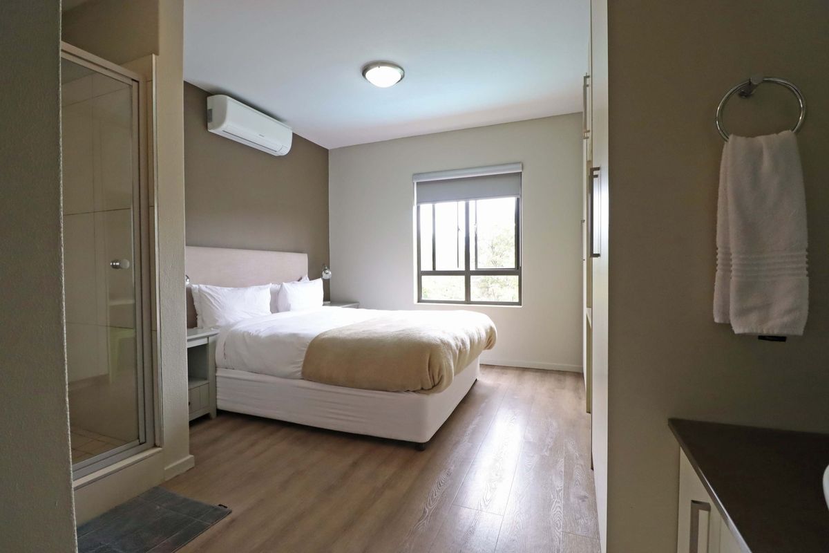A well-maintained bedroom featuring laminate flooring, built-in cupboards, an air conditioning unit, and an en-suite shower enclosure.