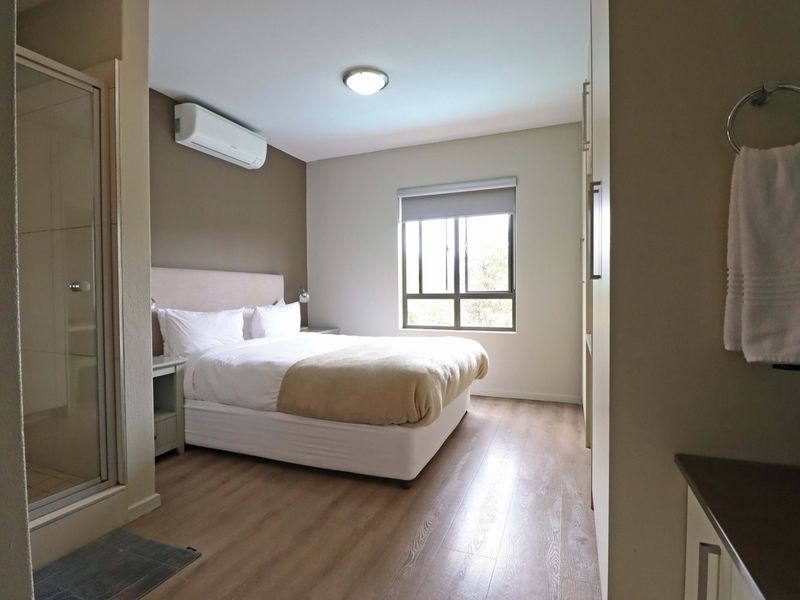 A well-maintained bedroom featuring laminate flooring, built-in cupboards, an air conditioning unit, and an en-suite shower enclosure.