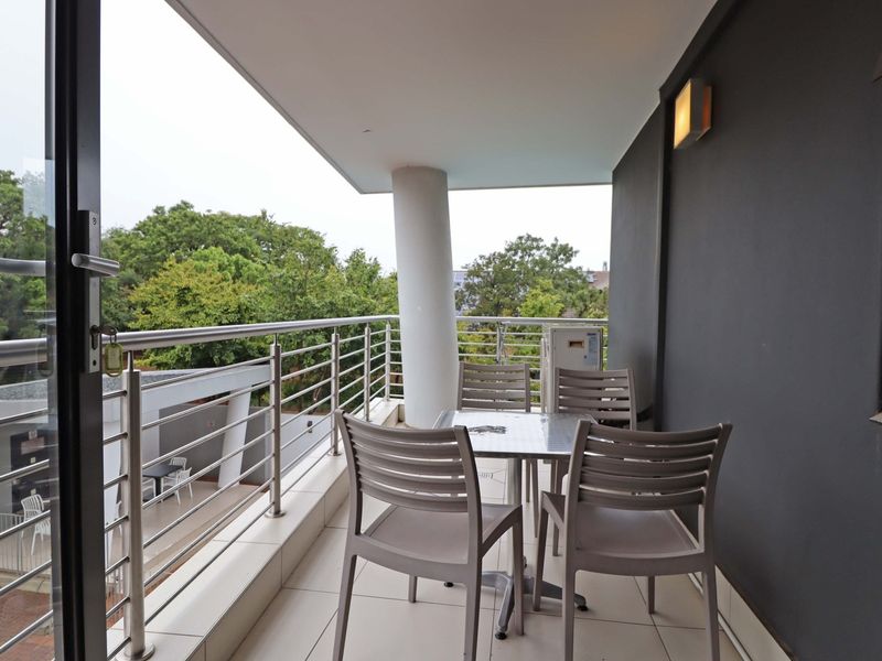 A covered balcony featuring tiled flooring, a stainless steel railing, and a structural column, offering an outdoor space for relaxation.