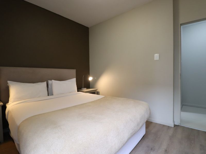A well-maintained bedroom featuring modern laminate flooring, a neutral color palette with a dark accent wall, and integrated lighting.