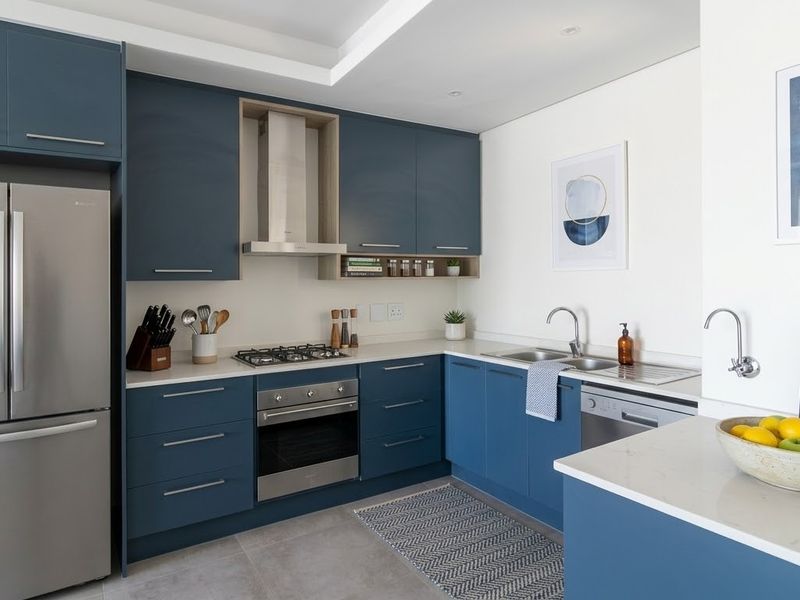 Modern kitchen featuring navy blue cabinetry, stone countertops, integrated stainless steel appliances, and a double bowl sink with a filtered water tap.