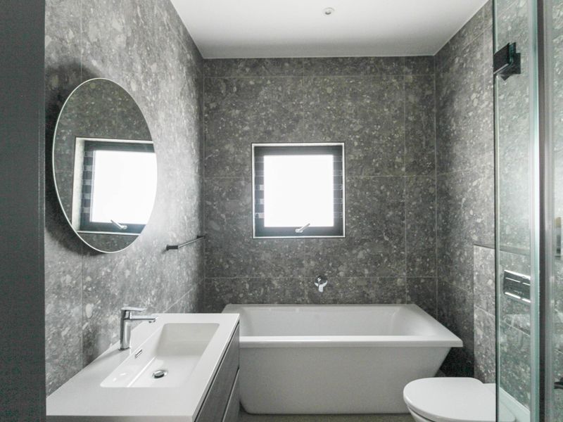 Modern bathroom featuring grey stone-look wall tiles, a built-in bathtub, a sleek vanity basin, and a glass-enclosed shower area.