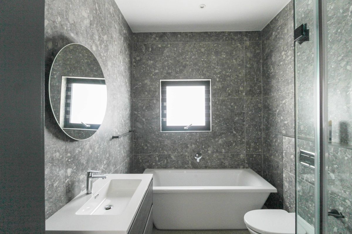 Modern bathroom featuring grey stone-look wall tiles, a built-in bathtub, a sleek vanity basin, and a glass-enclosed shower area.