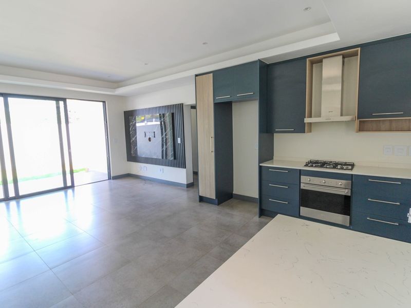 Modern open-plan kitchen and living area featuring sleek blue cabinetry, stone countertops, integrated appliances, and large sliding doors leading to the outdoors.