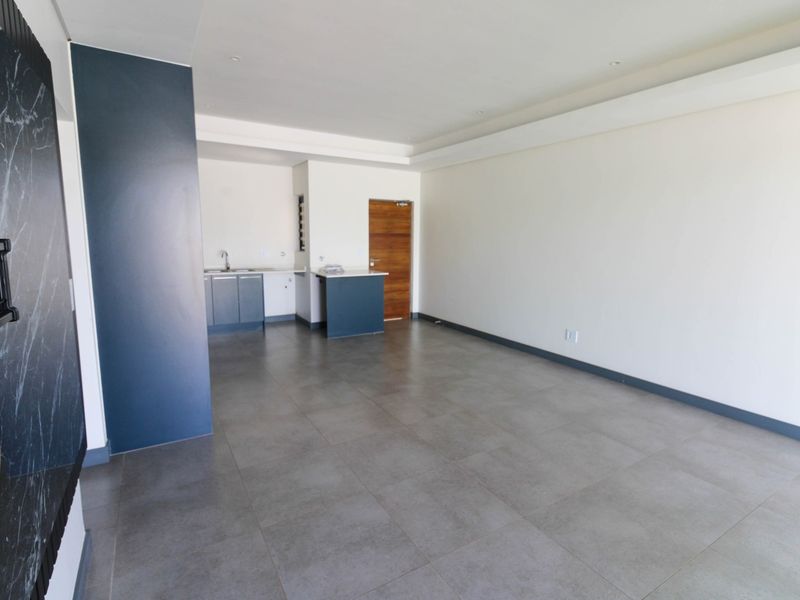 An open-plan living area featuring large format floor tiles, a modern kitchen corner with cabinetry, and a sleek built-in wall feature.