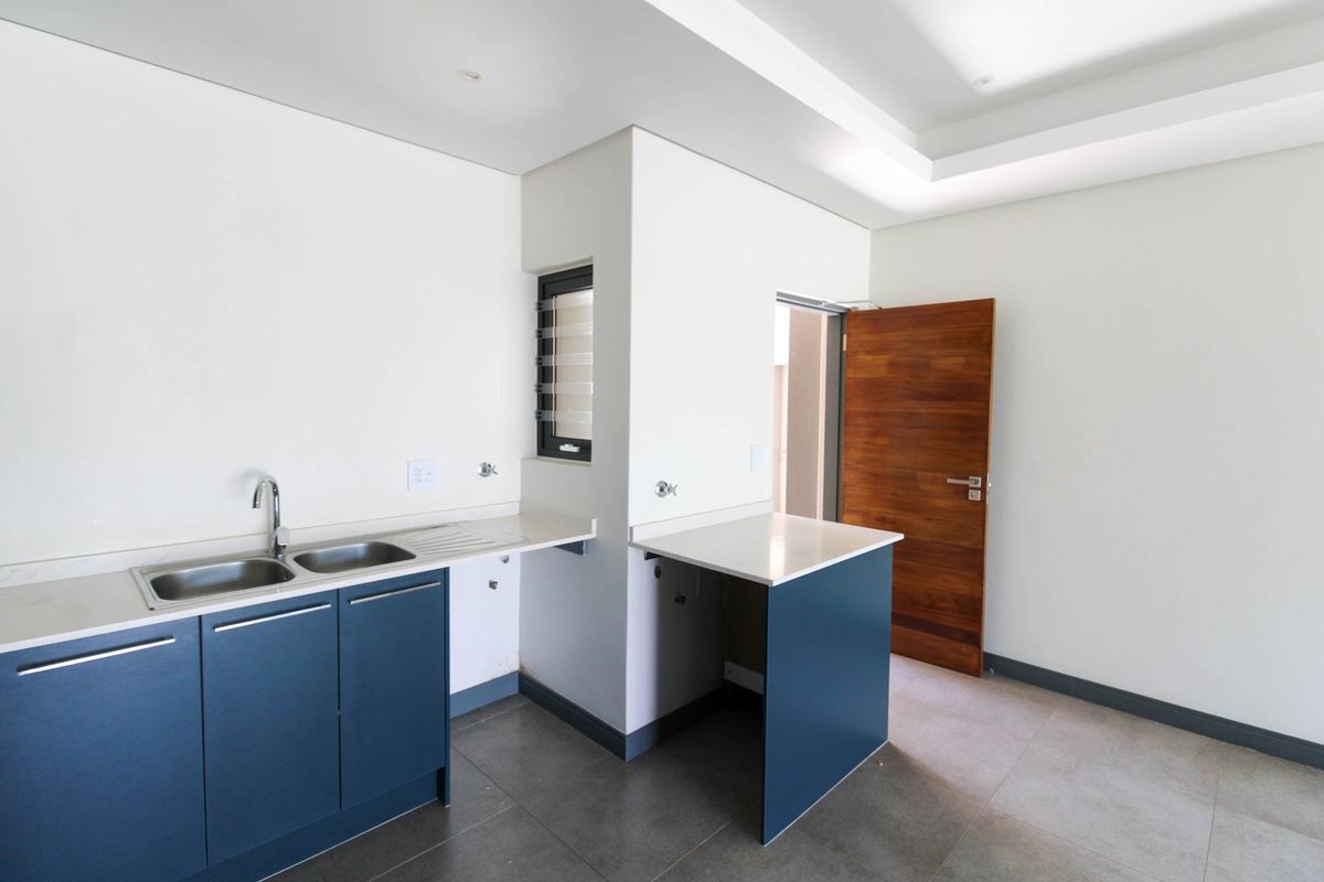 A modern, empty kitchen featuring blue cabinetry, stone countertops, a double basin sink, and tiled flooring with recessed ceiling lighting.