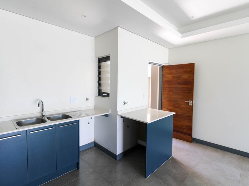 A modern, empty kitchen featuring blue cabinetry, stone countertops, a double basin sink, and tiled flooring with recessed ceiling lighting.