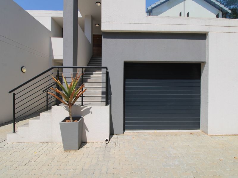 Modern apartment exterior featuring a paved driveway, a secure garage door, and an external staircase leading to the entrance.