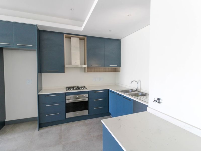 Modern kitchen featuring blue cabinetry, stone countertops, stainless steel appliances, and tiled flooring in a clean, contemporary layout.
