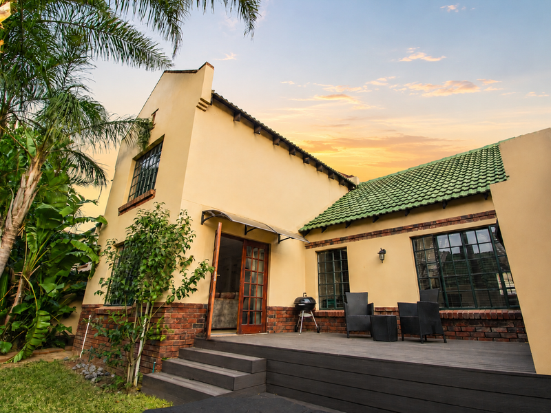 Rear view of the townhouse featuring a raised timber deck, brick and plaster facade, green tiled roof, and steel-framed windows overlooking a garden.