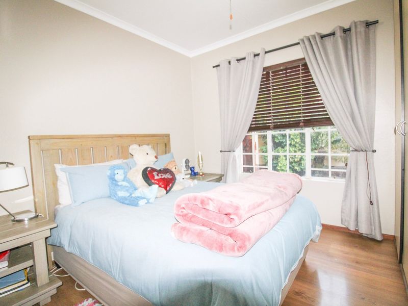 A cozy bedroom featuring laminate flooring, a built-in wardrobe, and a window fitted with wooden blinds and curtains.