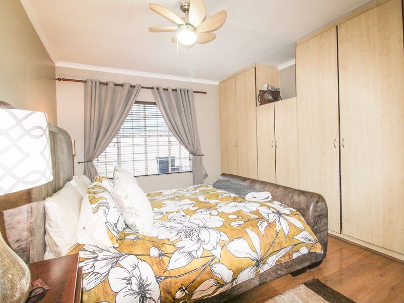 A bedroom featuring laminate flooring, built-in cupboards for storage, and a ceiling fan, providing a functional and comfortable living space.