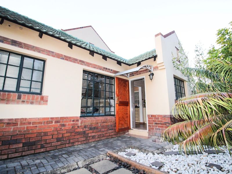 Rear exterior view of the townhouse featuring a brick facade, tiled roof, steel-framed windows, and a paved patio area leading to the entrance.