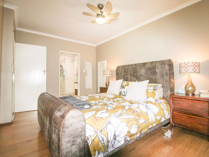 A well-maintained bedroom featuring laminate flooring, a ceiling fan, and convenient access to an en-suite bathroom.