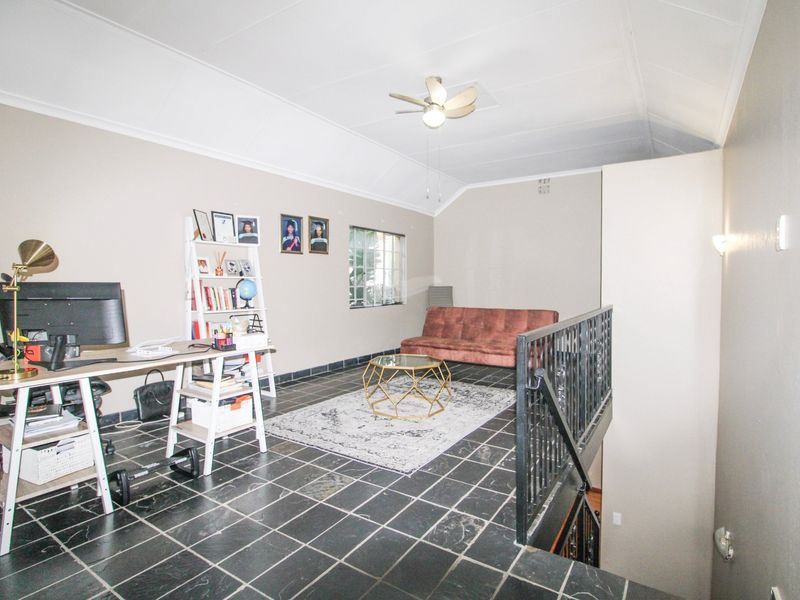 An open-plan mezzanine living area featuring vaulted ceilings, a ceiling fan, and dark tiled flooring with a metal safety balustrade overlooking the lower level.