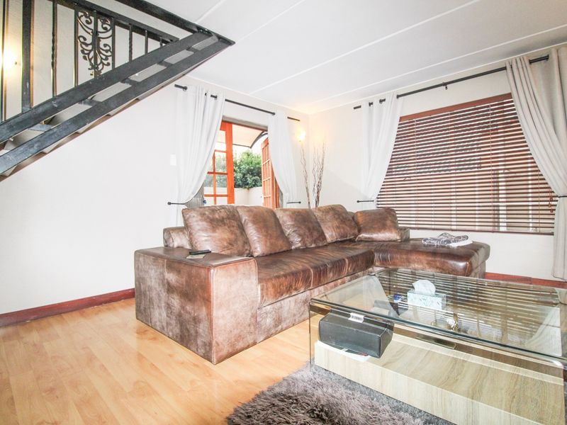 A comfortable living room featuring laminate flooring, a metal staircase, and access to the exterior through classic french doors.