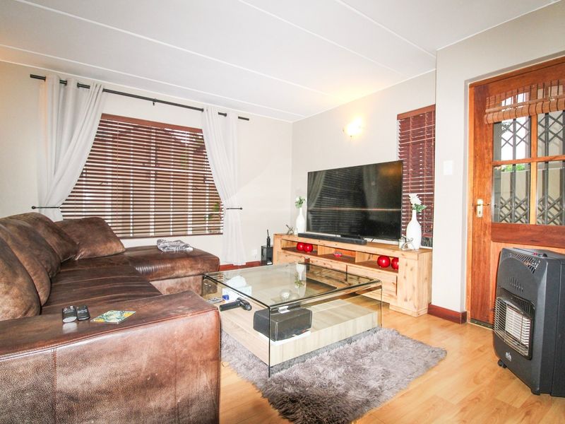 A comfortable living room featuring laminate flooring, wooden door with security gate, and venetian blinds, providing a functional and inviting space.