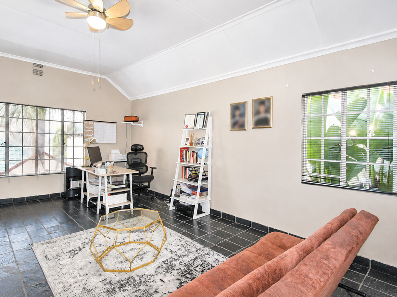 A bright living room featuring a vaulted ceiling, ceiling fan, dark tiled flooring, and large windows providing ample natural light.