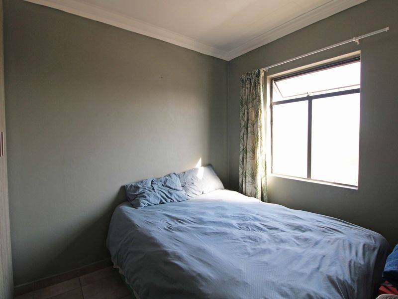A compact bedroom featuring tiled flooring, a built-in wardrobe, and decorative cornice detailing, offering a functional space with natural light.