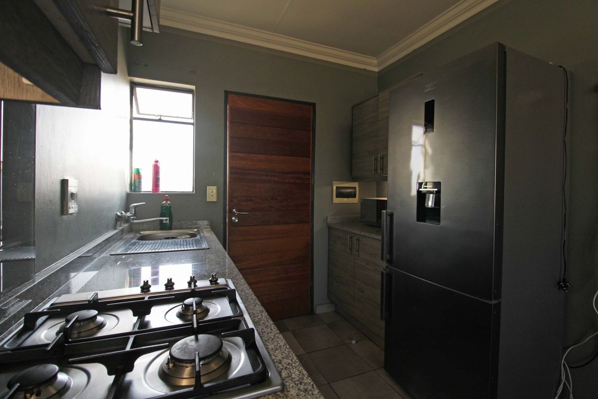 A functional kitchen featuring granite countertops, built-in cabinetry, a gas hob, and a stainless steel sink, finished with tiled flooring and a wooden door.