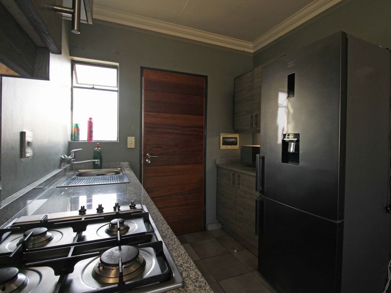 A functional kitchen featuring granite countertops, built-in cabinetry, a gas hob, and a stainless steel sink, finished with tiled flooring and a wooden door.