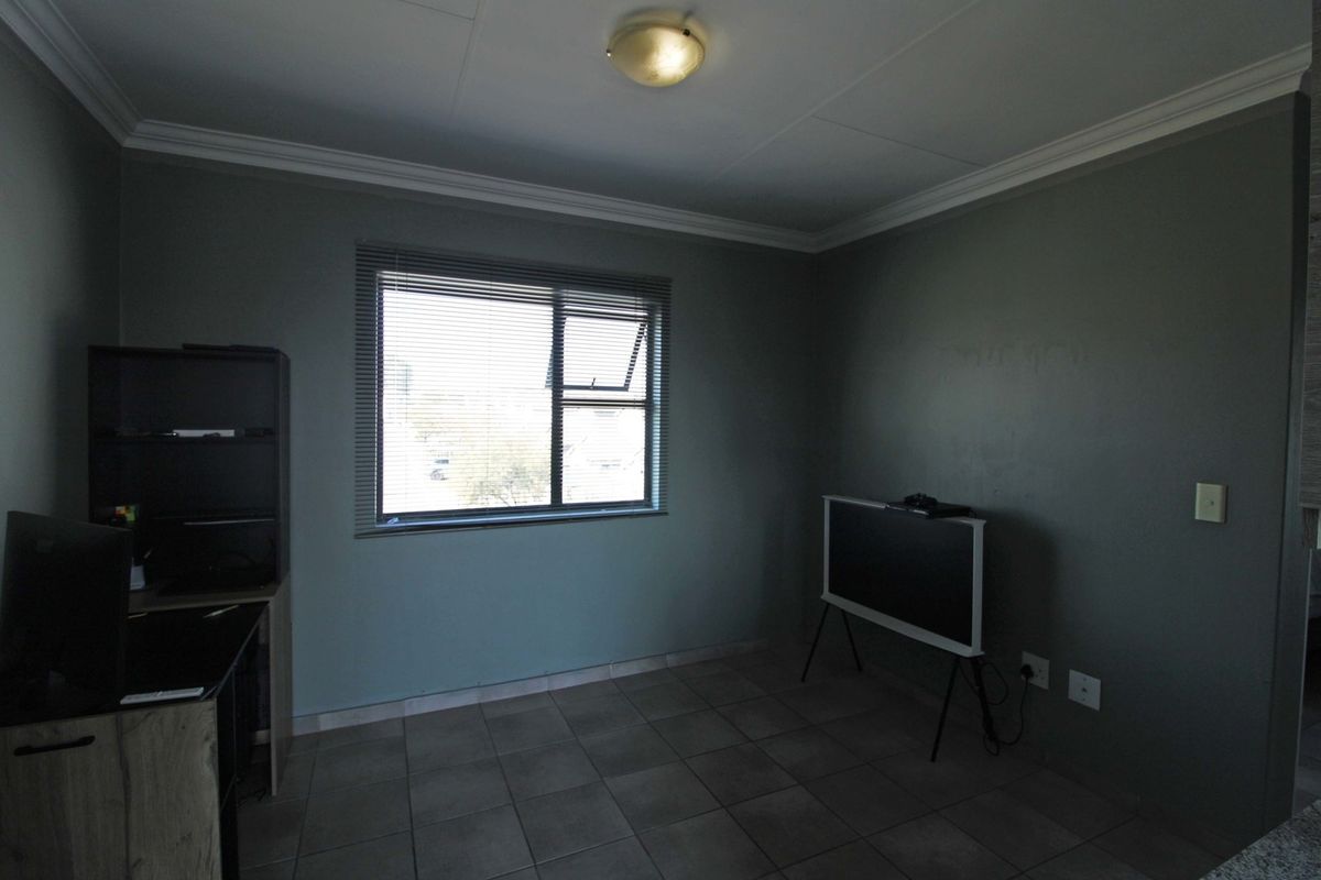 A neutrally painted living area featuring tiled flooring, ceiling cornicing, and a window fitted with venetian blinds.