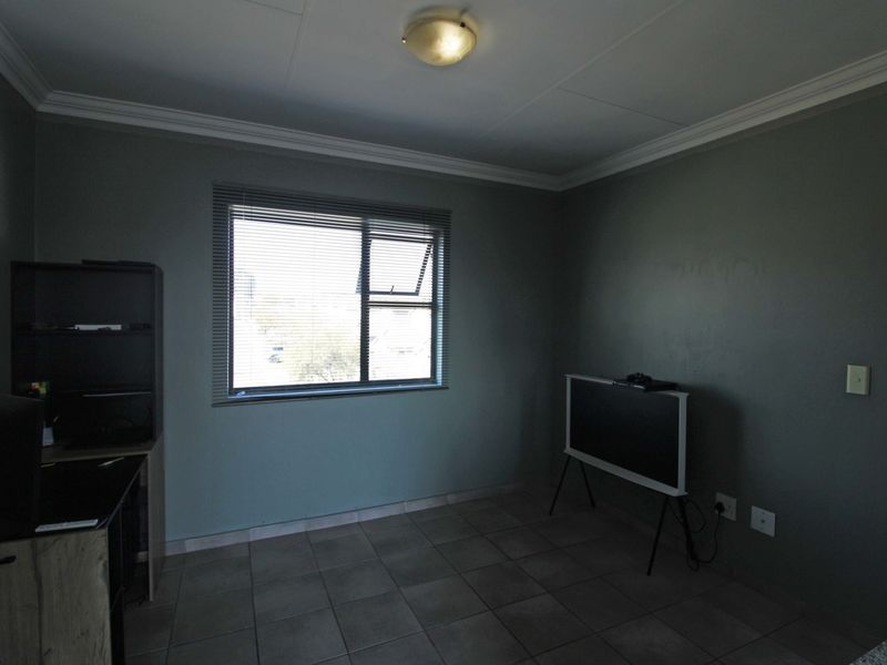 A neutrally painted living area featuring tiled flooring, ceiling cornicing, and a window fitted with venetian blinds.
