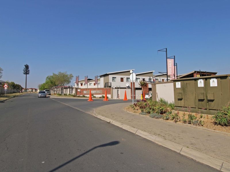 Street view showing the entrance and perimeter of the Sunset Place apartment complex with paved sidewalk and road access.