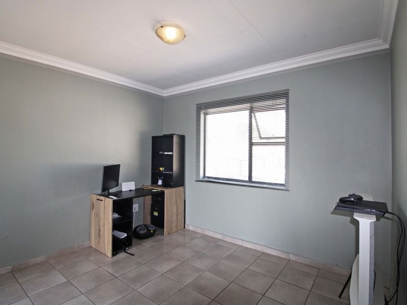 A functional office space featuring neutral wall paint, tiled flooring, decorative cornicing, and a window fitted with horizontal blinds.