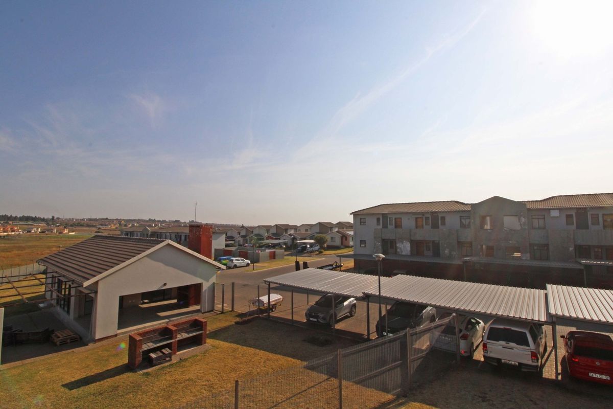 Aerial view of the apartment complex grounds featuring covered parking bays, a communal brick braai area, and surrounding residential neighborhood.