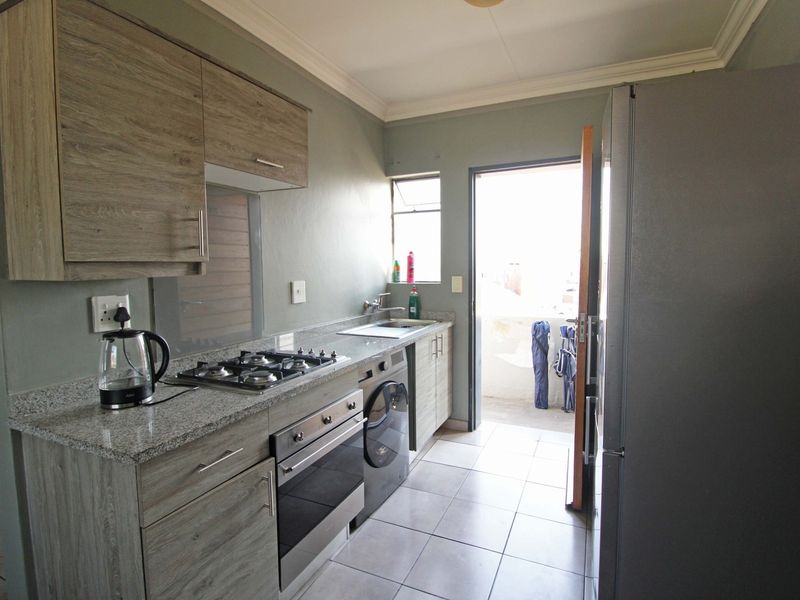 A functional kitchen featuring wood-look cabinetry, granite countertops, a gas hob, built-in oven, and tiled flooring with direct access to an outdoor area.