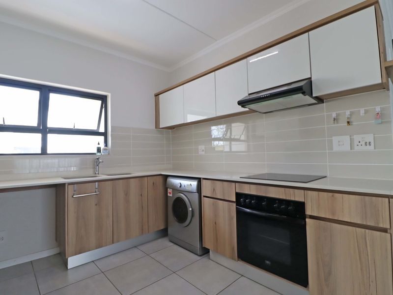 Modern kitchen featuring light wood-finish cabinetry, white upper cabinets, tiled backsplash, integrated appliances, and sleek countertops in a clean, well-maintained space.
